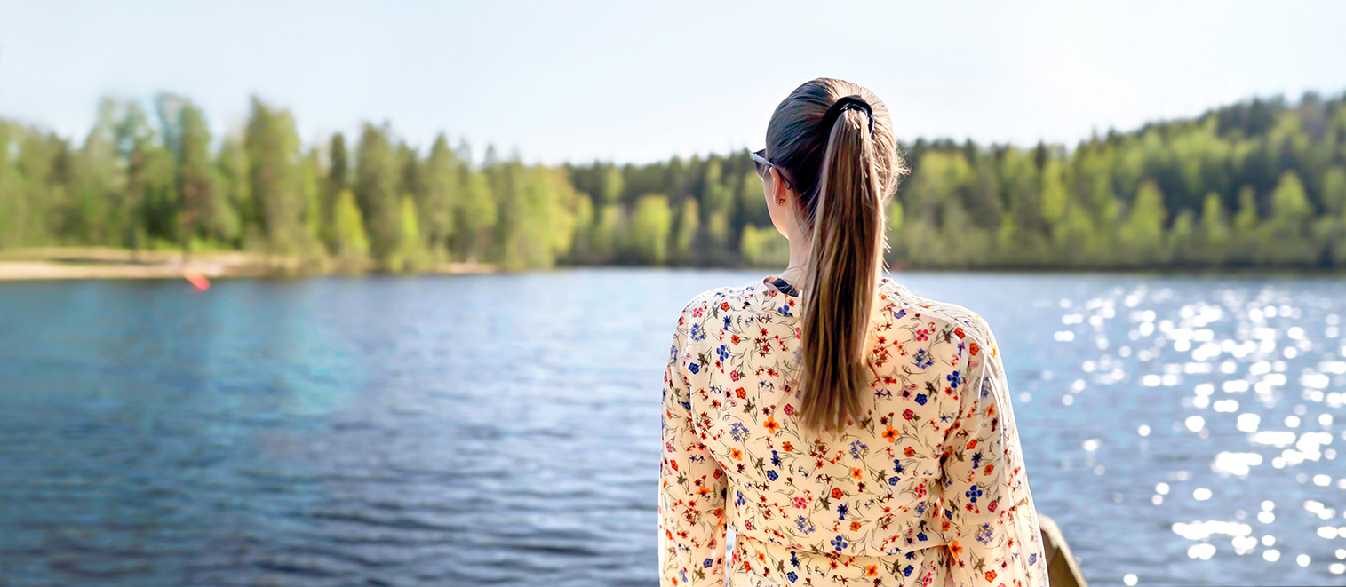 Nuori nainen ihastelemassa kesäistä järvinäkymää